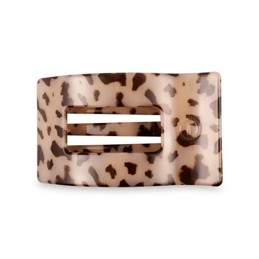 A rectangular hair claw clip with a glossy tortoiseshell pattern in beige and brown, featuring a central cutout with two horizontal white bars and a small circular brand logo on the right side.