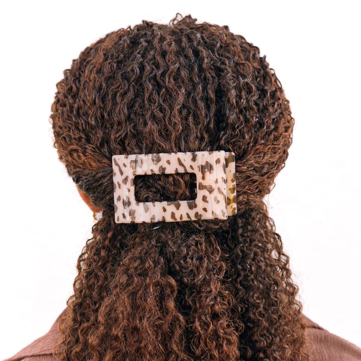 Person with curly hair wearing a leopard print hair clip on a white background