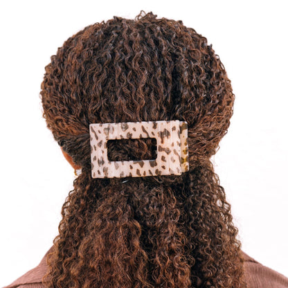 Person with curly hair wearing a leopard print hair clip on a white background