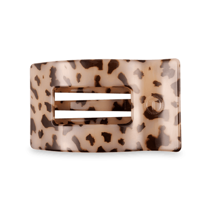 A rectangular hair claw clip with a glossy tortoiseshell pattern in beige and brown, featuring a central cutout with two horizontal white bars and a small circular brand logo on the right side.